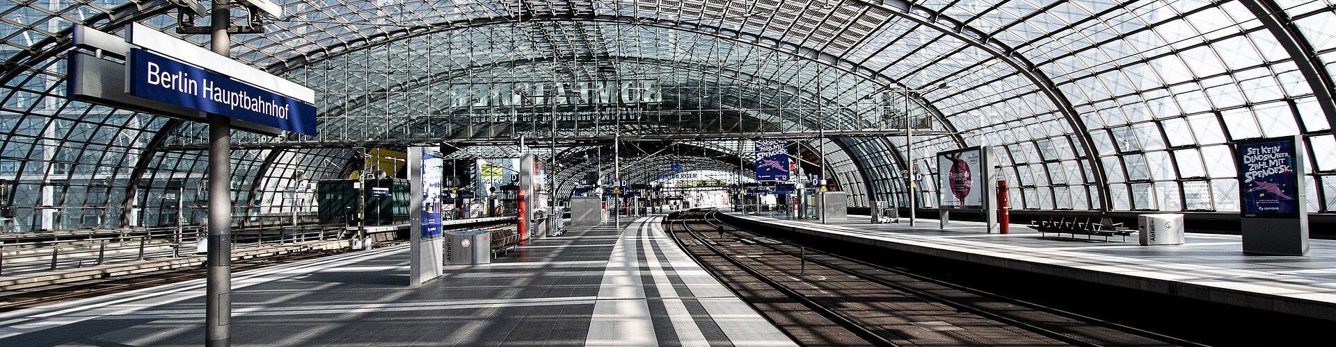 Na zdjęciu widać nowoczesny, przeszklony peron stacji kolejowej z imponującym zadaszeniem o konstrukcji łukowej.